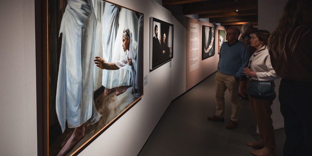 Bezoekers bekijken schilderijen van Egbert Modderman in een sfeervolle museumgang met houten balken en ingetogen verlichting.