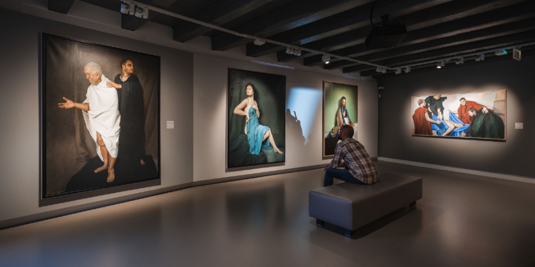 Bezoeker bekijkt figuratieve schilderijen in een museumzaal met werken van Egbert Modderman tegen grijze wanden en spotverlichting.