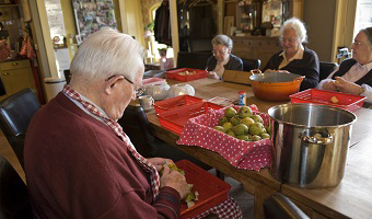 Ouderen aan keukentafel. Ze schillen appels.