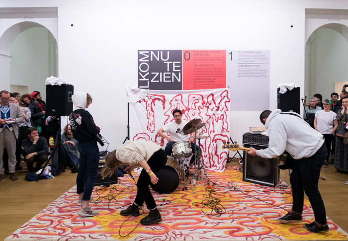 Band met studenten in museum, pubiek er omheen, drums, gitaren, headbangen