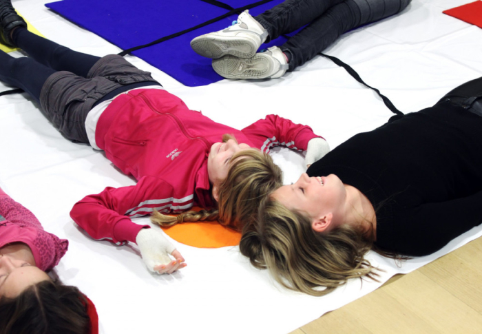 kinderen liggen op de grond tijdens een workshop, op een witte ondergrond met vormen van kunststroming 'De Stijl'