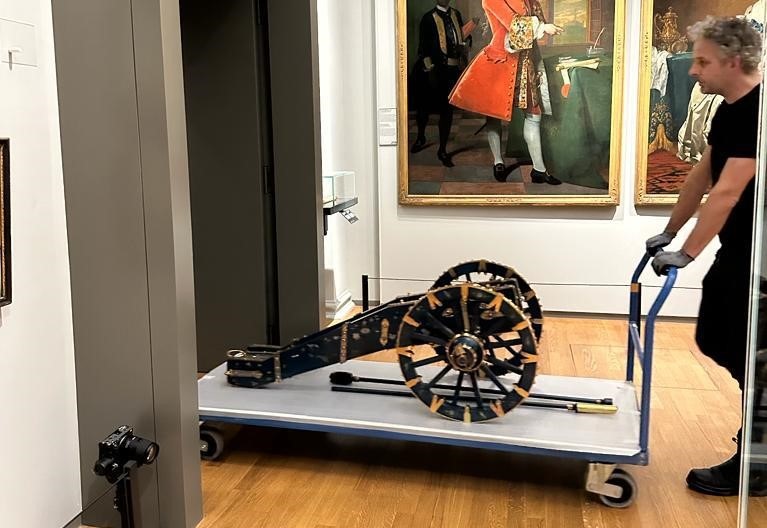 A canon is being transported on a cart by a man, and two paintings hang in the background