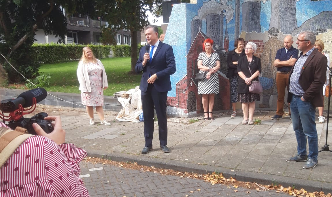 Foto: Gitte Kroes. Zicht op gezelschap mensen rond een man die hen toespreekt met microfoon in de hand. Links onder op de rug gezien, persoon die daar een foto van neemt. Foto: Gitte Kroes. Zicht op gezelschap mensen rond een man die hen toespreekt met microfoon in de hand. Links onder op de rug gezien, persoon die daar een foto van neemt.